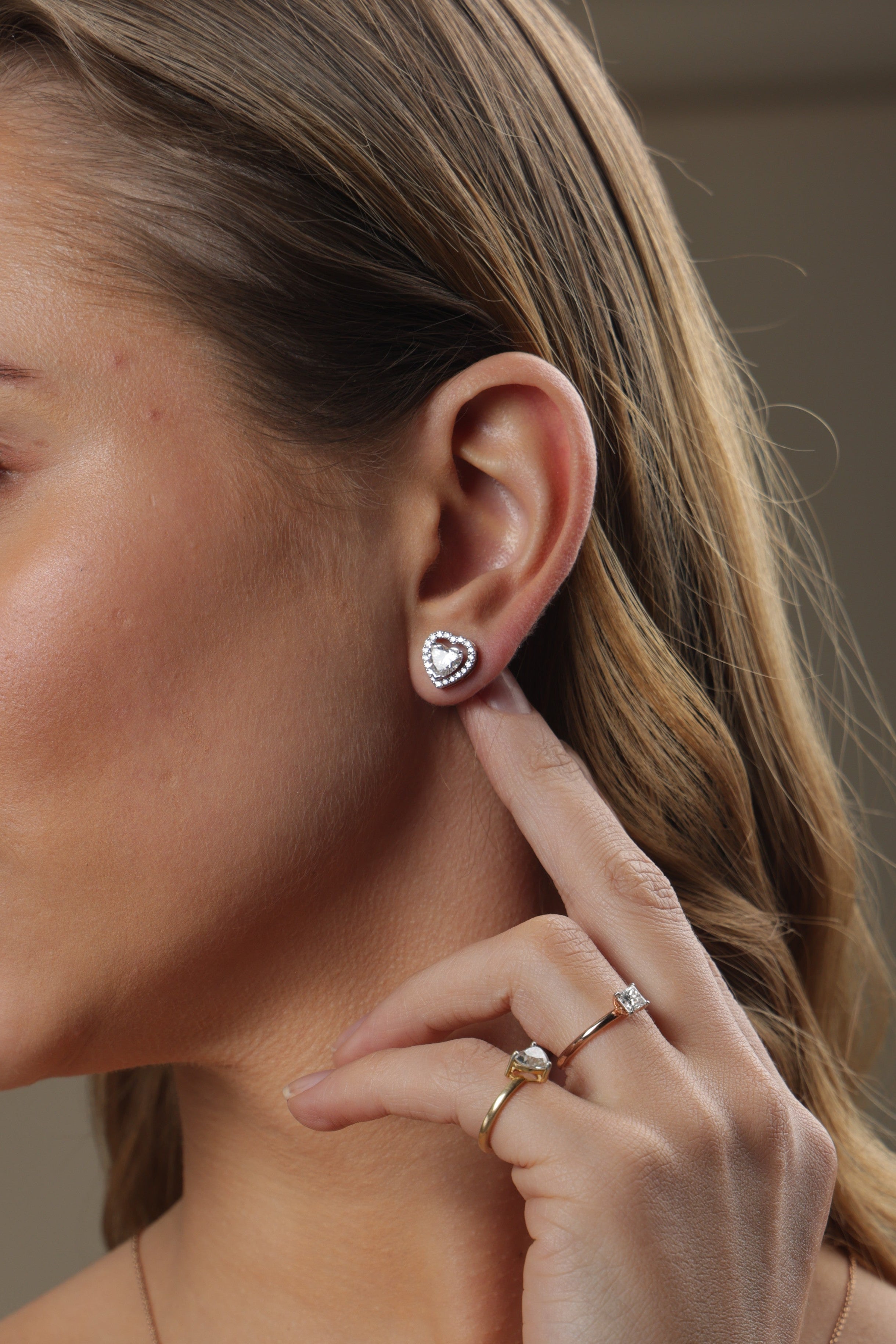 Woman wearing a diamond earring and ring, with a neutral background