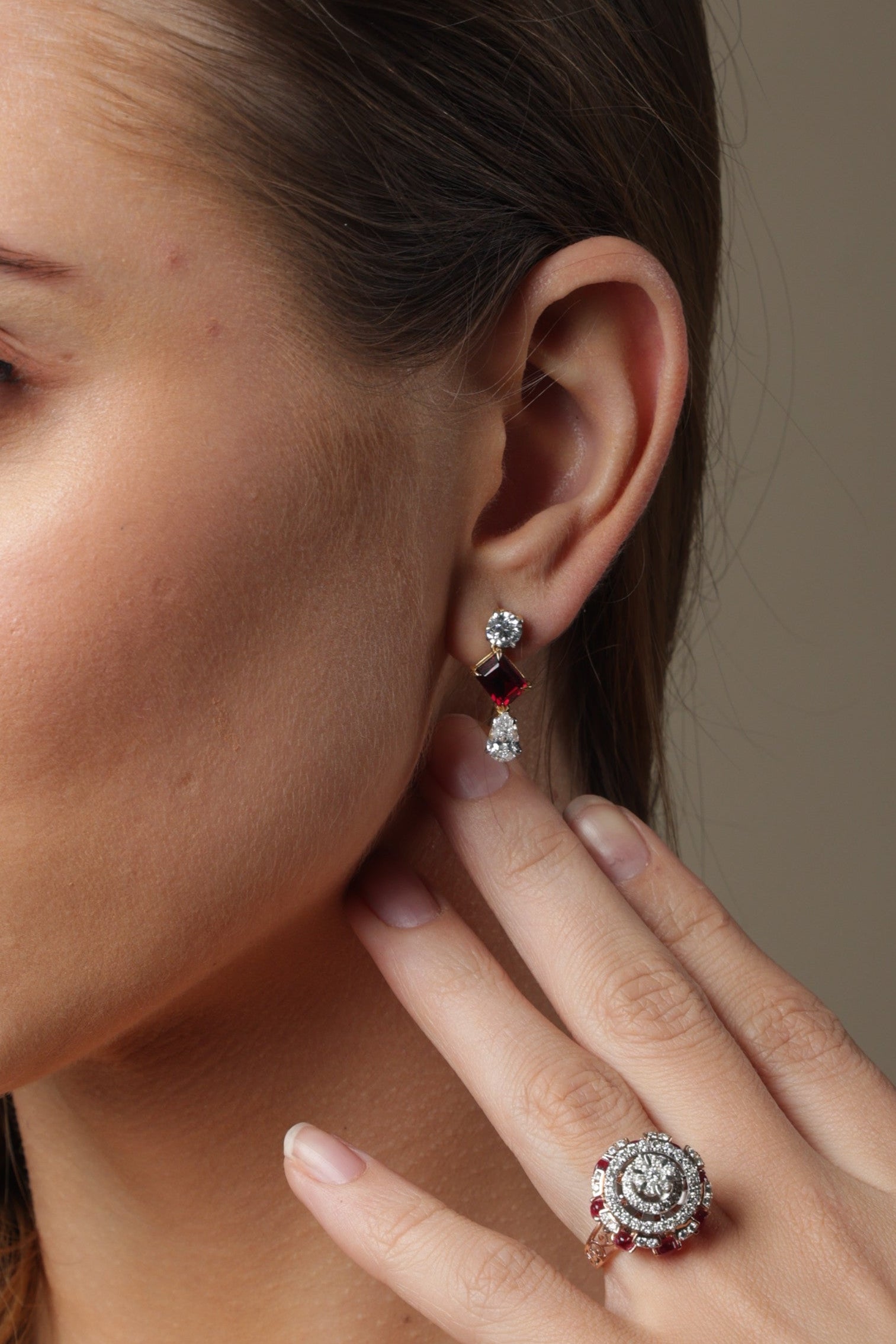 Woman wearing jewelry, including earrings and a ring, against a neutral background
