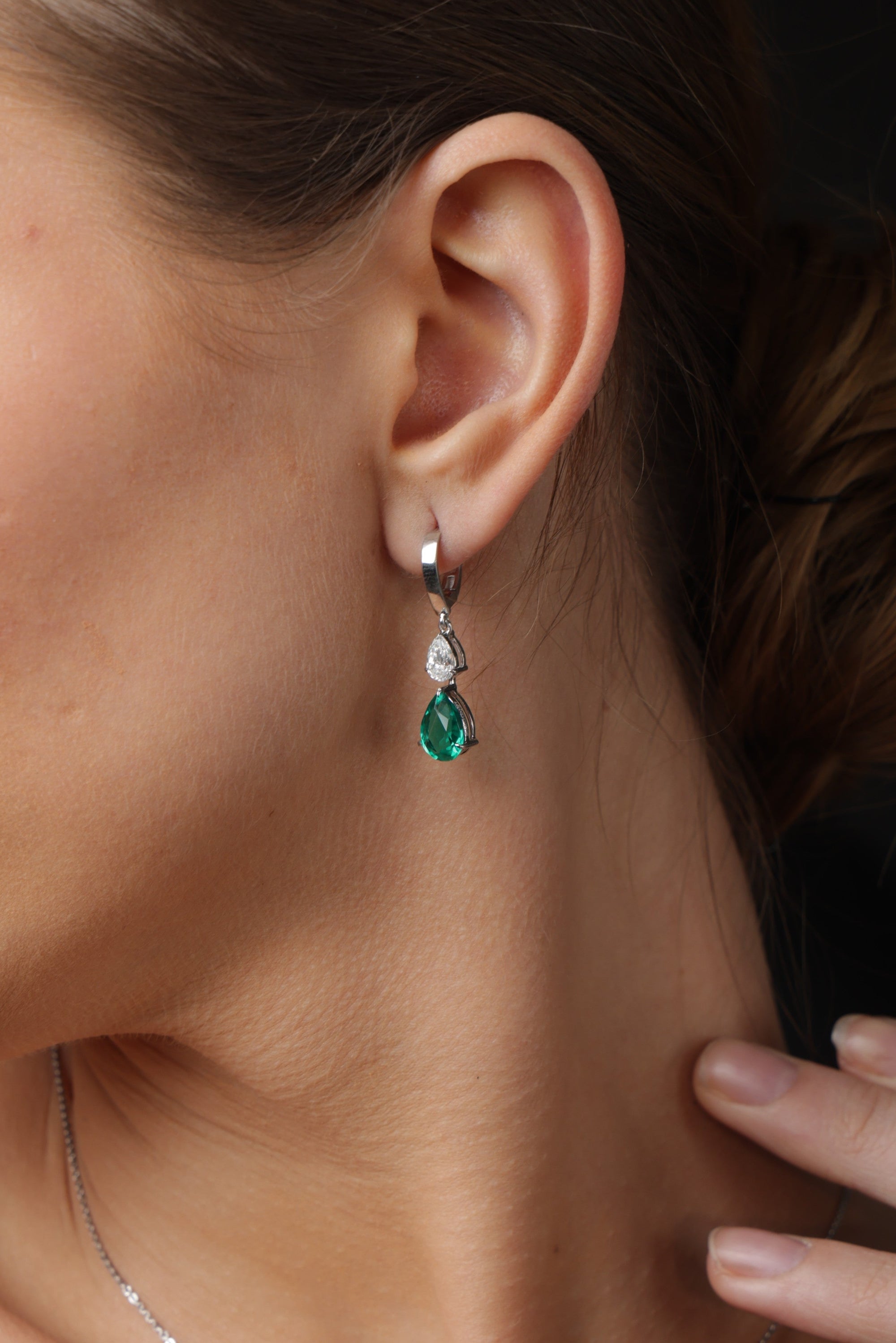 Close-up of a woman wearing emerald green earrings and necklace with a dark background