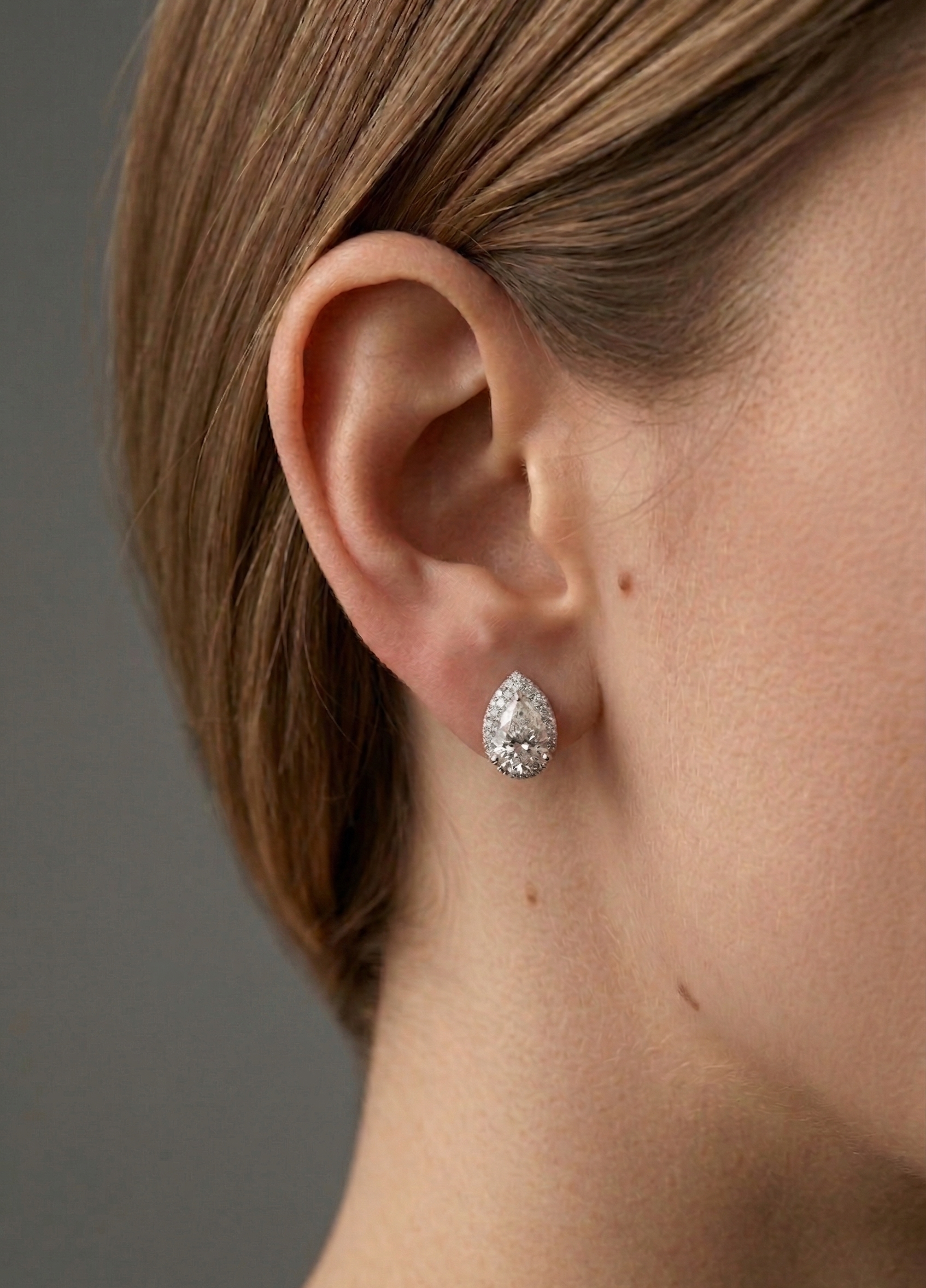 Close-up of an ear wearing a diamond earring with a neutral background