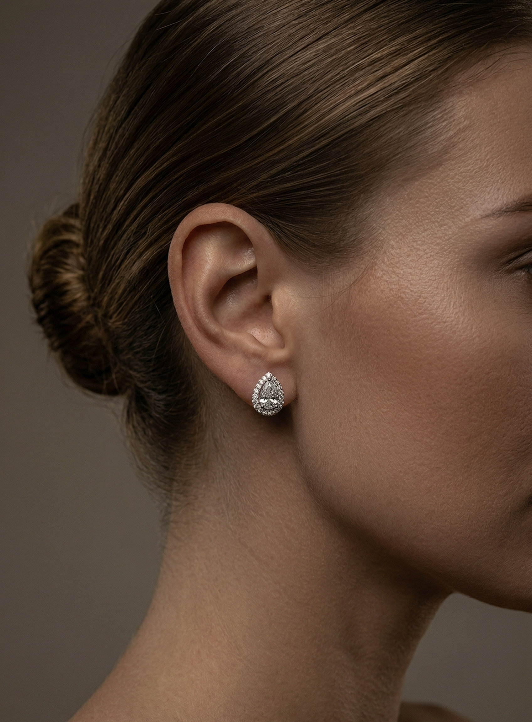Close-up of a woman's ear wearing a diamond earring against a neutral background