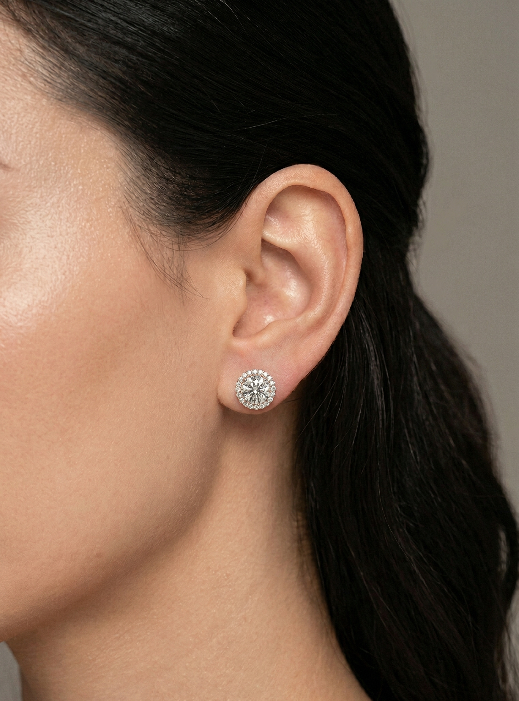 Close-up of a person wearing a diamond stud earring with a neutral background